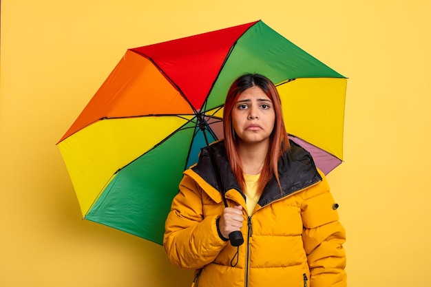 不幸な表情と泣き声で悲しみと泣き言を感じるヒスパニック系の女性。雨と傘のコンセプト