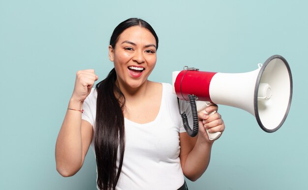 Hispanic woman feeling shocked, excited and happy, laughing and celebrating success, saying wow!