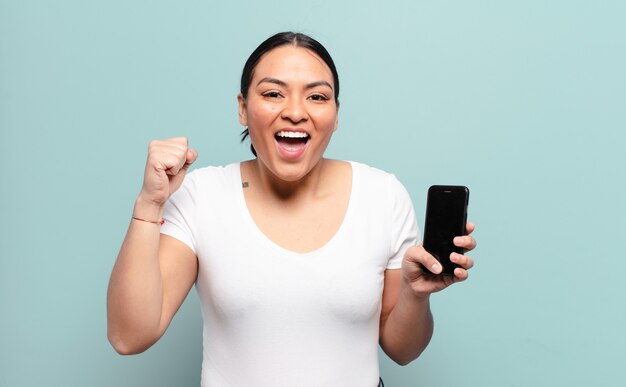 Hispanic woman feeling shocked, excited and happy, laughing and celebrating success, saying wow!