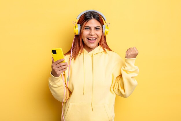 hispanic woman feeling shocked,laughing and celebrating success. headphones and smartphone concept