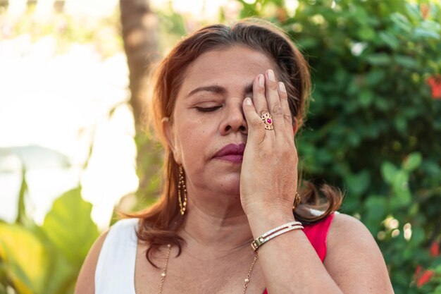 Donna ispanica di cinquant'anni con i capelli rossi copre il viso con la mano