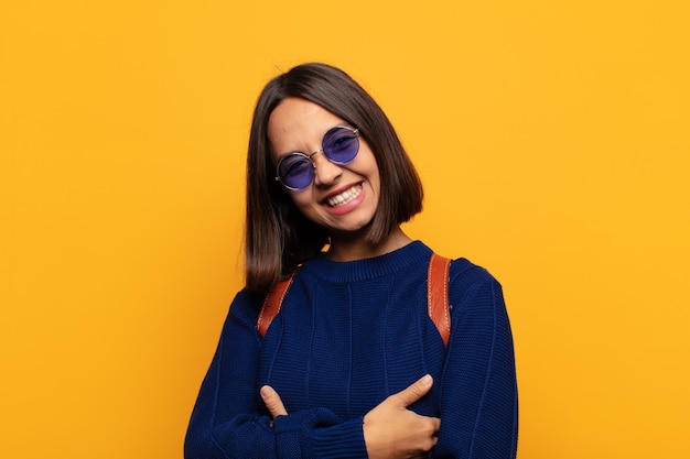 Hispanic woman laughing happily with arms crossed, with a relaxed, positive and satisfied pose