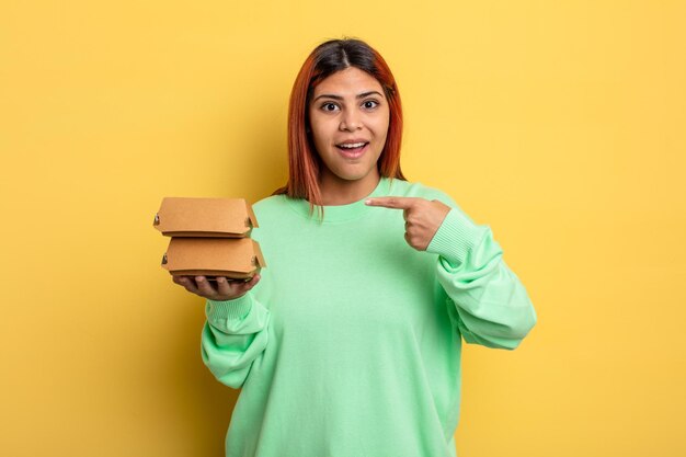 Hispanic woman looking excited and surprised pointing to the side take away burgers concept