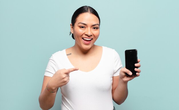 Hispanic woman looking excited and surprised pointing to the side and upwards to copy space