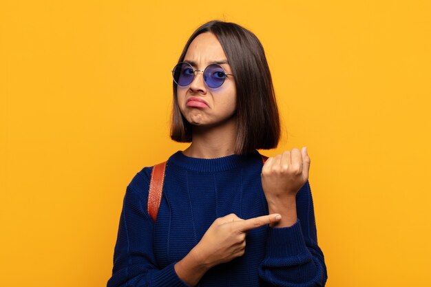 Hispanic woman looking impatient and angry, pointing at watch, asking for punctuality, wants to be on time