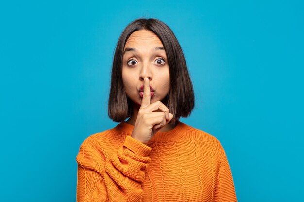 Hispanic woman looking serious and cross with finger pressed to lips demanding silence or quiet, keeping a secret