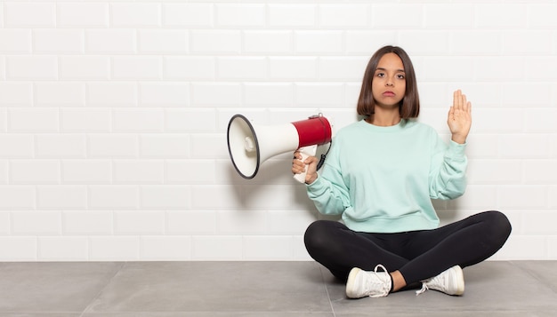 Hispanic woman looking serious, stern, displeased and angry showing open palm making stop gesture