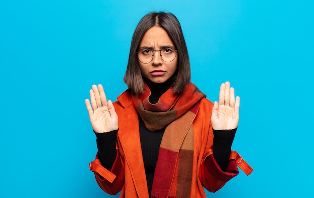 Hispanic woman looking serious, unhappy, angry and displeased forbidding entry or saying stop with both open palms