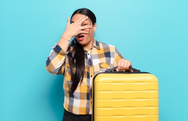 Hispanic woman looking shocked, scared or terrified, covering face with hand and peeking between fingers