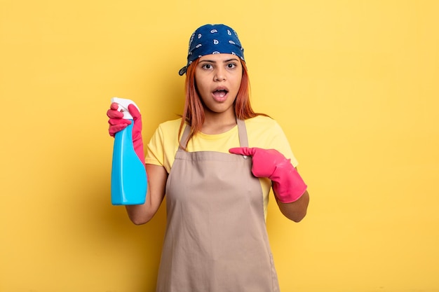 Hispanic woman looking shocked and surprised with mouth wide open, pointing to self. cleaning and housekeeper concept