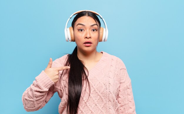 Hispanic woman looking shocked and surprised with mouth wide open, pointing to self