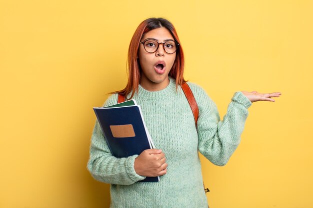 hispanic woman looking surprised and shocked, with jaw dropped holding an object. student concept