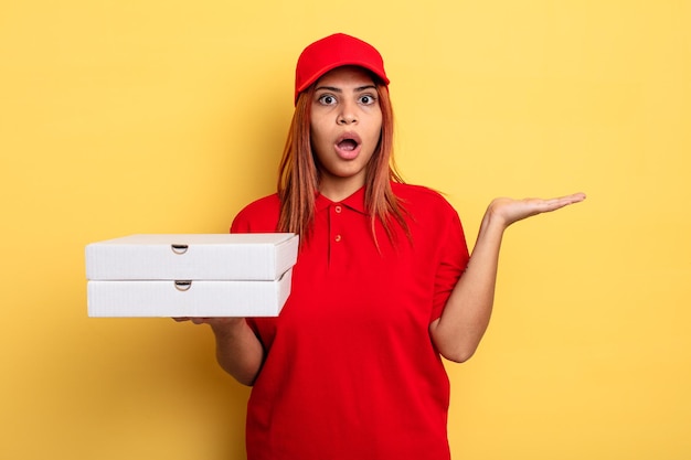 Hispanic woman looking surprised and shocked, with jaw dropped holding an object. take away deliver concept