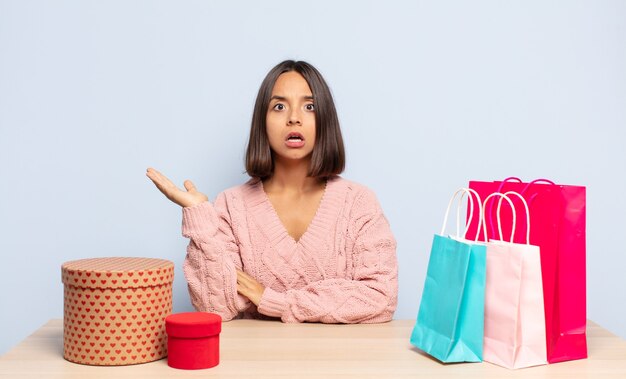 Hispanic woman looking surprised and shocked, with jaw dropped holding an object with an open hand on the side