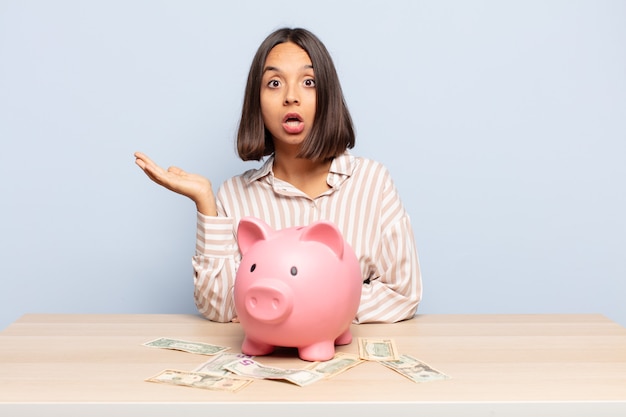 Hispanic woman looking surprised and shocked, with jaw dropped holding an object with an open hand on the side