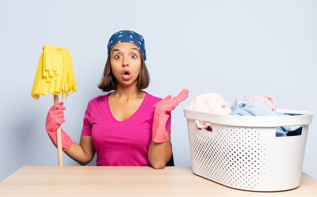 Hispanic woman looking surprised and shocked, with jaw dropped holding an object with an open hand on the side