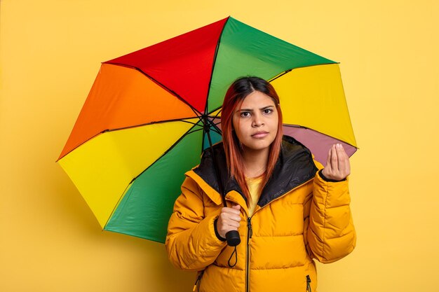 Hispanic woman making capice or money gesture, telling you to pay. rain and umbrella concept