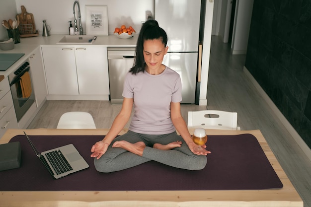 Hispanic woman meditating with beer near laptop