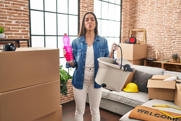 Hispanic woman moving to a new home cleaning the floor looking at the camera blowing a kiss being lovely and sexy. love expression.