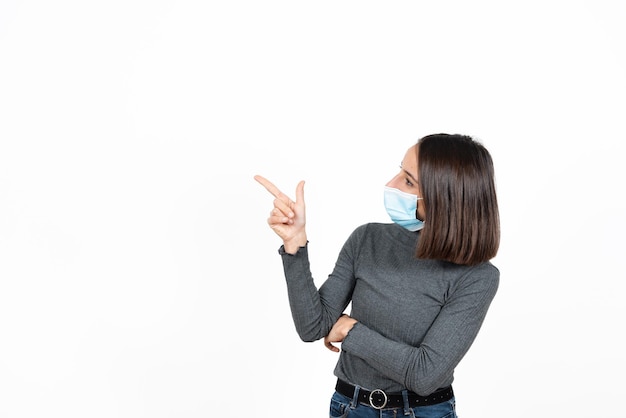 Hispanic woman pointing to copy space while wearing a medical face mask