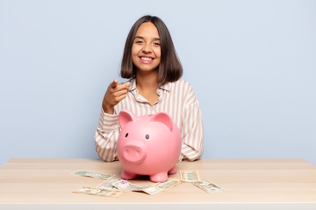 Hispanic woman pointing at front with a satisfied, confident, friendly smile, choosing you