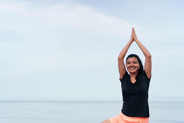 Hispanic woman practicing yoga, stretching her body on the beach