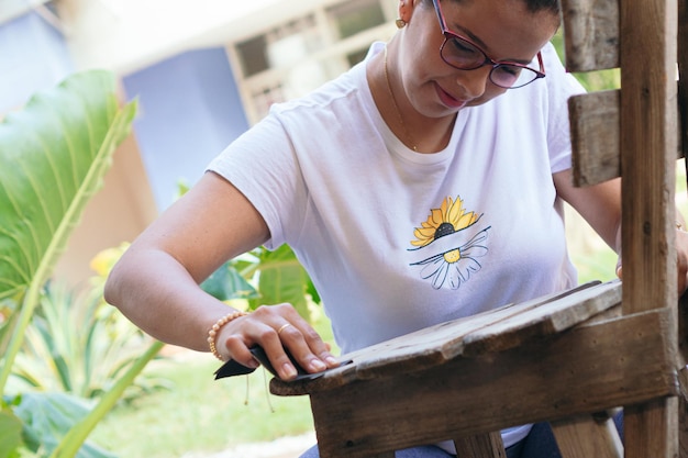 Hispanic woman restoring old chair outdoors on patio, working