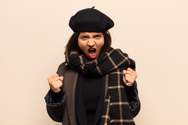 Hispanic woman shouting aggressively with an angry expression or with fists clenched celebrating success