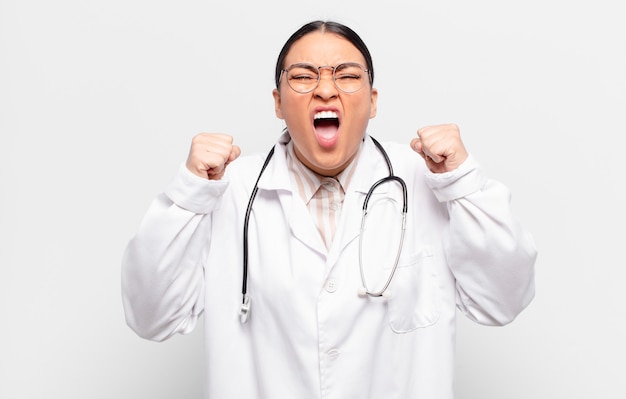 Hispanic woman shouting aggressively with an angry expression or with fists clenched celebrating success