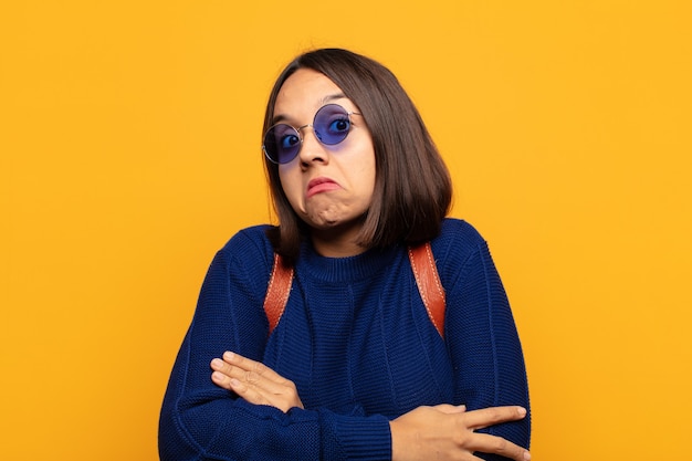 Hispanic woman shrugging, feeling confused and uncertain, doubting with arms crossed and puzzled look