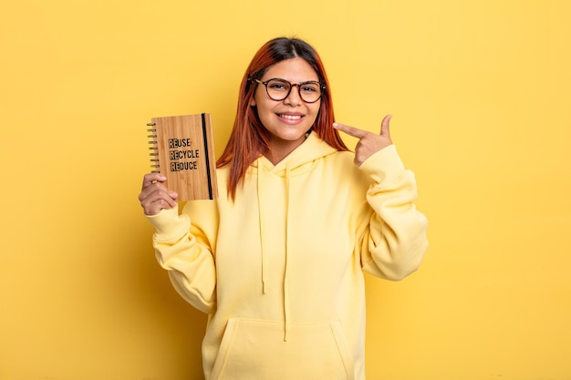 Hispanic woman smiling confidently pointing to own broad smile. recycle concept