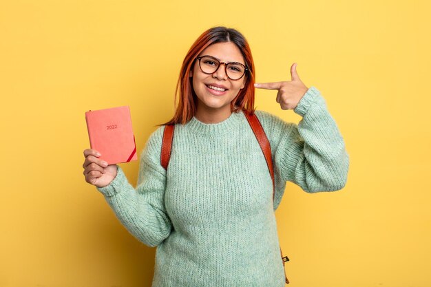 Hispanic woman smiling confidently pointing to own broad smile. student and calendar concept