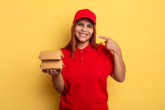 Hispanic woman smiling confidently pointing to own broad smile take away deliver concept