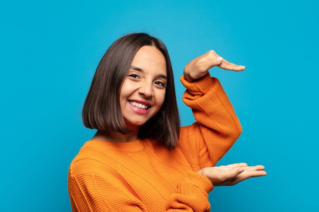 Hispanic woman smiling, feeling happy, positive and satisfied, holding or showing object or concept on copy space