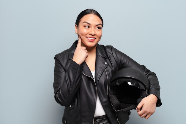 Hispanic woman smiling happily and daydreaming or doubting, looking to the side