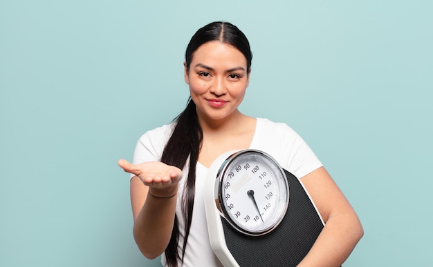 Hispanic woman smiling happily with friendly, confident, positive look, offering and showing an object or concept