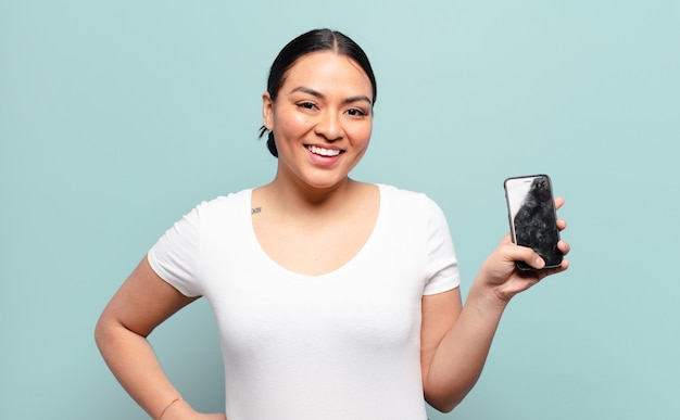 Hispanic woman smiling happily with a hand on hip and confident, positive, proud and friendly attitude