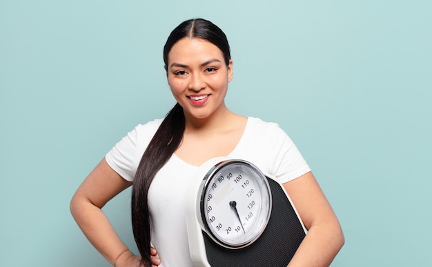 Hispanic woman smiling happily with a hand on hip and confident, positive, proud and friendly attitude