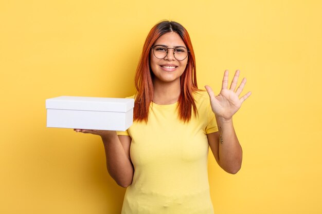 Hispanic woman smiling and looking friendly, showing number five. empty packaging concept