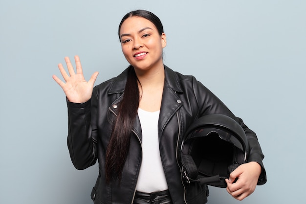 Hispanic woman smiling and looking friendly, showing number five or fifth with hand forward, counting down