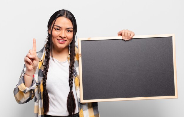 Hispanic woman smiling and looking friendly, showing number one or first with hand forward, counting down