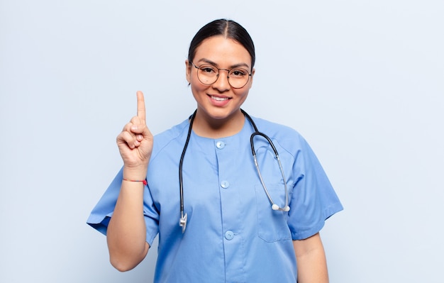 Hispanic woman smiling and looking friendly, showing number one or first with hand forward, counting down