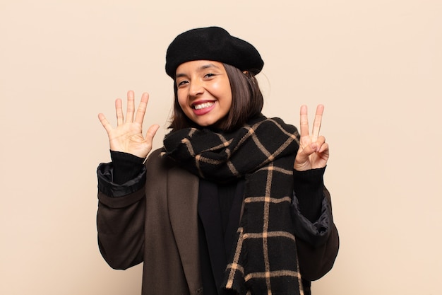 Hispanic woman smiling and looking friendly, showing number seven or seventh with hand forward, counting down