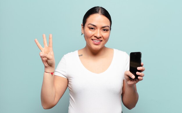 Hispanic woman smiling and looking friendly, showing number three or third with hand forward, counting down