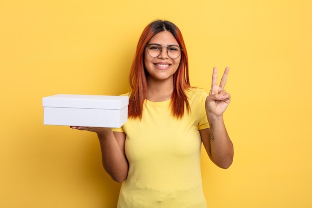 Hispanic woman smiling and looking friendly showing number two empty packaging concept