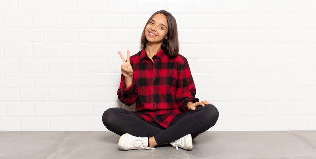 Foto donna ispanica che sorride e che sembra felice, spensierata e positiva, gesticolando vittoria o pace con una mano