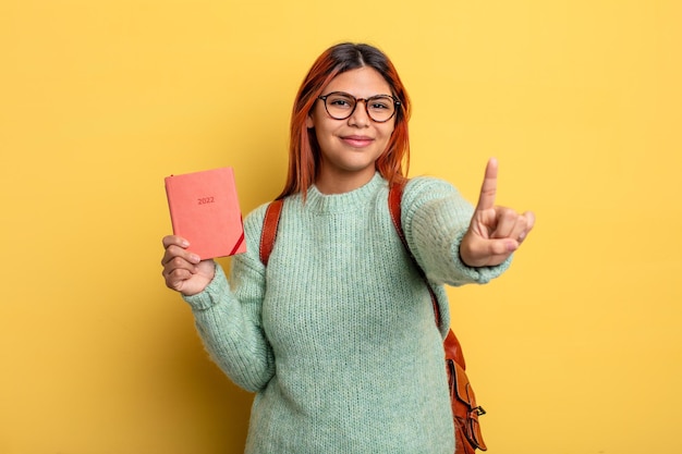 Hispanic woman smiling proudly and confidently making number one. student and calendar concept