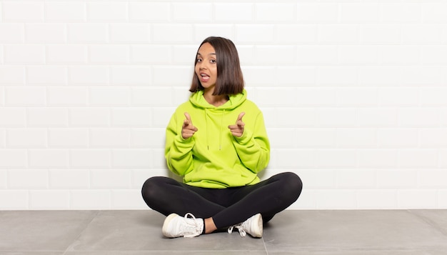 Hispanic woman smiling with a positive, successful, happy attitude pointing to the camera, making gun sign with hands