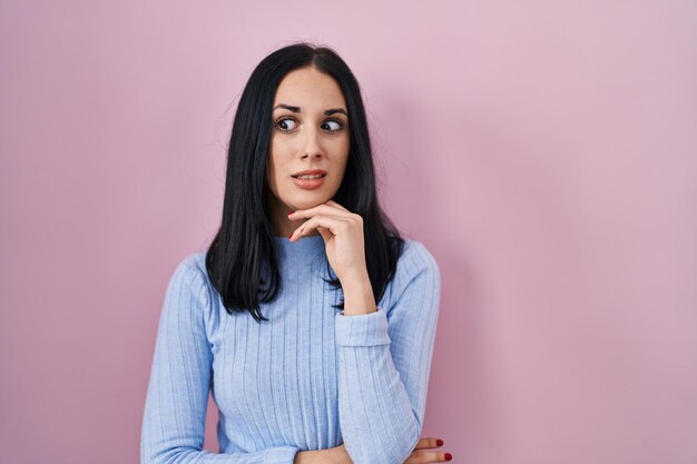 Photo hispanic woman standing over pink background thinking worried about a question concerned and nervous with hand on chin