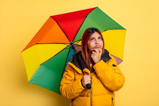 ヒスパニック系の女性が考え、疑わしく、混乱していると感じています。雨と傘のコンセプト